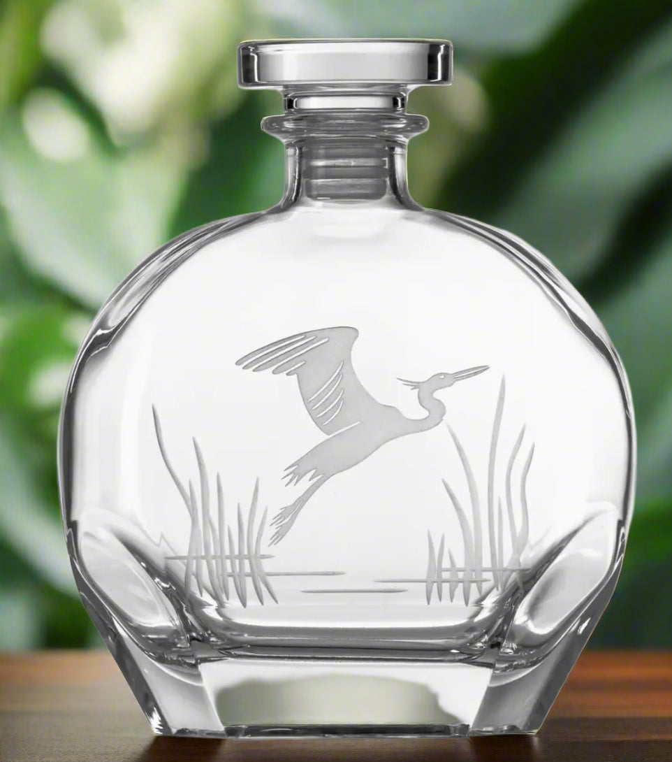 Clear glass decanter with engraved design of a heron on a white background
