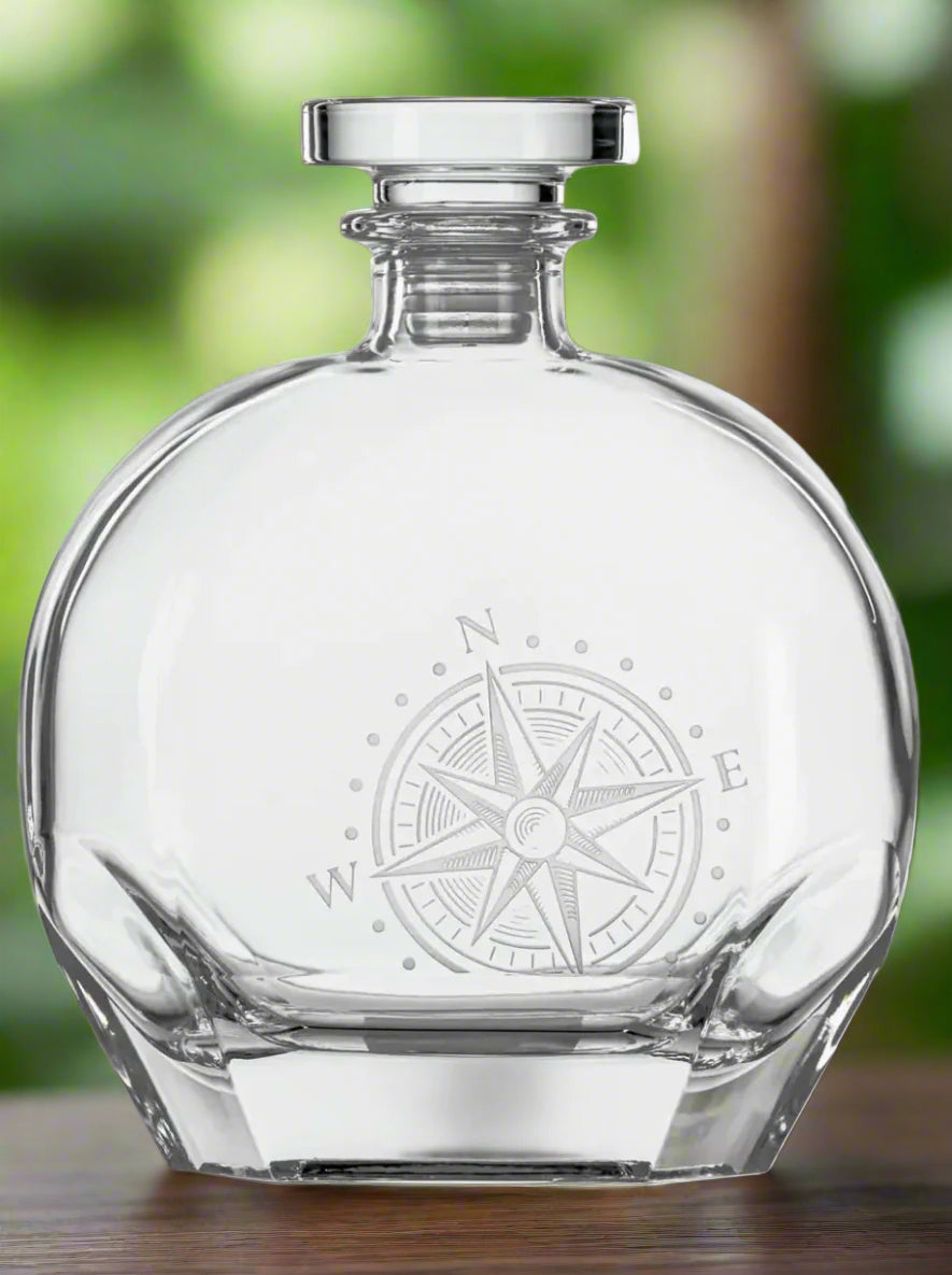 Clear glass decanter with compass engraving on a white background